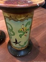 Close-up of one candleholder showing Asian-inspired artwork with a figure standing and a bird beneath botanical scrolls.