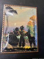 Front angled view of the antique picture showing the silhouetted figures and curved glass.