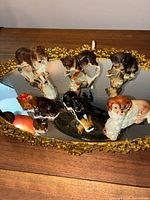 Photo of seven antique porcelain dog figurines arranged on a decorative mirrored tray with gold floral trim, showing various dog breeds in different poses.