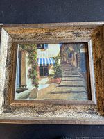 Framed print showing a village street scene with staircase and flowers.