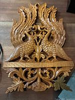 Top view of Balinese wooden carved plaque showing two birds with spread wings flanking a central floral design, revealing detailed carving and natural wood finish.