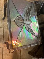 Top angled view of rectangular stained glass panel depicting a flying dove with iridescent glass showing pearl colors and light reflections.