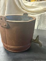 Side view of cast iron vessel showing cylindrical shape, rust surface and top open rim