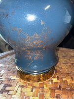 Close-up photo showing powder blue ceramic base with intricate gold floral designs and speckled glazed finish.