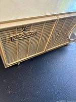 Close-up of the beige plastic front grille of the radio showing the 'Dual Speakers' insignia with crown emblem.