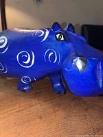Close-up photo of the left side of the blue hand carved hippopotamus with white spiral patterns and painted facial details.