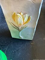 Front view of the rectangular floral design wall piece showing embossed yellow flower with green stem on a beige base.