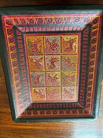 Overall view of the rectangular wooden art piece with geometric and animal motif patterns in red, yellow, and black shades on brown background.