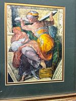 Framed print showing the Libyan Sibyl figure with colorful robes, seated and holding a tablet, mounted on dark green matting and gold-tone frame.