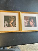 Pair of framed prints depicting angelic children with wings, both double matted and set in gold textured frames on a black surface.