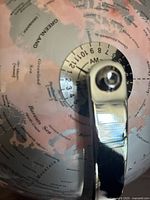 Photo showing salmon colored globe with visible country names and time zone dial on chrome stand.