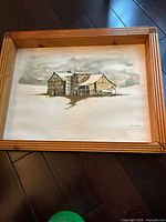 Full view of the framed Ronald Woodall picture featuring a barn in a snowy field under a cloudy sky.