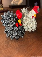 Photo showing both handcrafted turkeys, one black and one white, on a wooden surface.