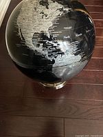 Globe showing North America, part of South America, with clear white geographical text on black background, standing on dark wood floor.