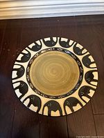 Top view of the round plate showing its beige center and elephant motif border in black and white.