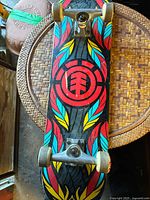 Top view of Element Feather Flow skateboard deck showing colorful feather-themed graphic design with Element logo in red, blue, and yellow on black background along with metal trucks and wheels attached.
