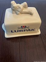 Top and side view of the ceramic Lurpak butter dish with "Douglas," the butter man figurine on the lid and Lurpak logo on the side.