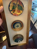 Framed case containing three round art plates arranged vertically, showing full set and mounting