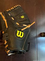Photo of one Wilson baseball glove primarily black leather with tan lacing and yellow 'W' logo.