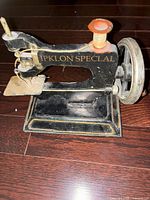 Front and side view of the vintage toy sewing machine money bank showing the body with 'IPKLON SPECIAL' text and the hand crank spool.