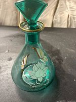 Front and side view of an emerald green glass vase with gold rim and floral design.