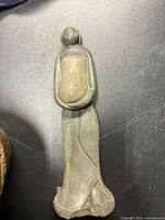 Vintage figurine or sculpture with grayish-green hue, viewed from front on black surface.