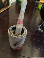 Photo showing the vintage wooden mortar and pestle set with visible red paint accents and overall wear