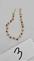 Full view of 14K gold flower design bracelet with red and clear gemstones
