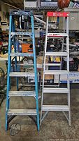Full view of two aluminum ladders side by side (Werner blue ladder and Davidson silver ladder) in workshop environment.