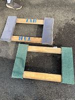 Top view of two moving dollies, showing wooden frames with carpet padding and caster wheels underneath. One dolly has green padding, the other gray.