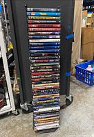 Stack of 40 DVD movies on a black metal stand with wheels, showing spines of DVDs with titles.