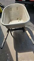 Front view of the wheelbarrow showing the plastic tray and wooden handles, with surface dirt visible.