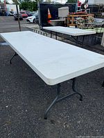 Full view of the 8-foot white folding picnic table showing plastic top and metal legs.