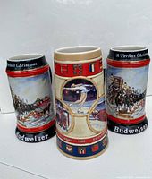 Front and partial side view of three Budweiser collectible beer steins, two with winter carriage scenes and one Calgary 1988 Olympic commemorative.