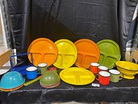 Full set of colorful enamelware on display including divided plates, mugs, bowls, colander, and utensils.