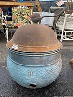 Front and side view of weathered decorative metal pot with blue embossed pattern and rusty domed lid with knob.