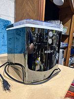 Front angle view of black and silver Igloo ice maker with power cord showing.