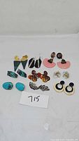 Lot of 10 pairs of assorted earrings laid out on white background. Various colors and shapes visible.