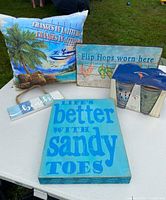 Photo of all items showing the pillow, beach signs, and pint glasses with holder on a white table outdoors.