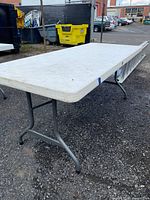 Full length of white folding picnic table with metal legs, outdoor setting.