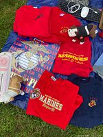 Five sweatshirts laid out, four red and one navy, with US Marines logos along with two dog figurines for scale.
