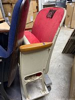 Side view of the vintage theater chair showing red upholstery, wooden armrest, and beige metal base with footrest.