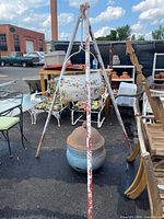 Full front view of white metal tripod with hanging cauldron and separate decorative pot behind