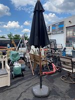 Full view of closed black patio umbrella standing on weighted base showing surrounding outdoor items.