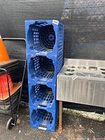 Four blue plastic stackable water jug holders stacked vertically with grid side design and circular jug cutouts