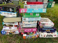 Stacked assortment of puzzle boxes showing multiple titles and piece counts including 750 piece, 500 piece, and 1000 piece puzzles from various brands.