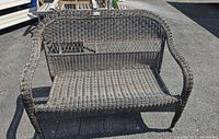 Front view of resin wicker settee bench showing woven resin wicker in brown tones and rounded backrest.