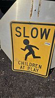 Full view of yellow metal sign reading 'SLOW CHILDREN AT PLAY' with black silhouette of child running.