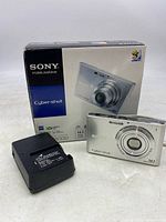 Sony Cyber-shot DSC-W330 camera front and box with battery charger on table