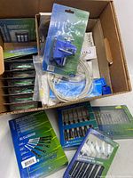 Overview of box containing packaged Velleman precision and electronic screwdriver sets, cables, and crimping tool.